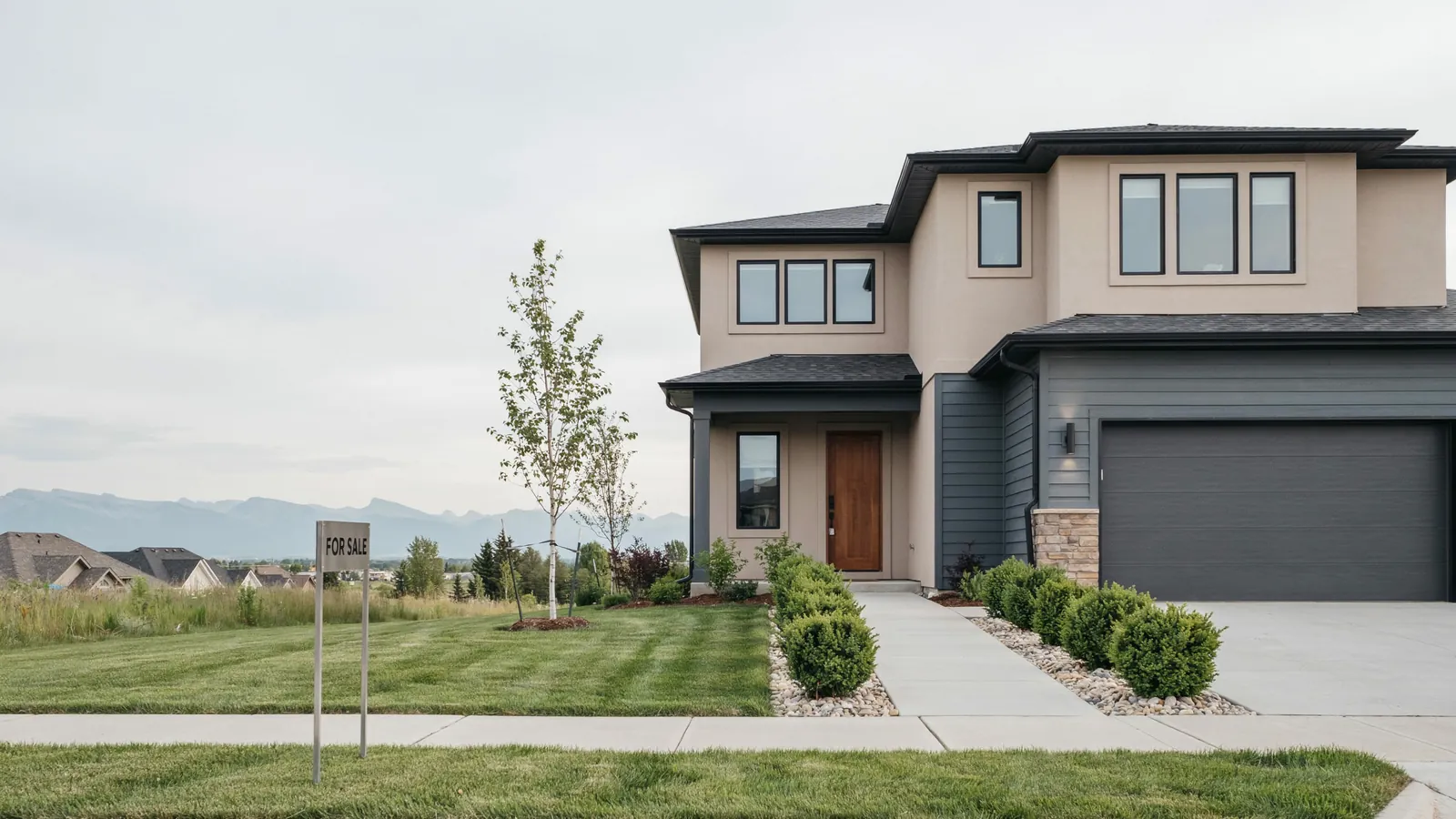 A modern two storey home with mountains behind it and a for sale sign on the lawn, the Calgary foreclosure guide